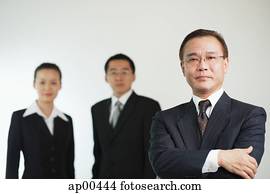 Businessman with arms crossed, looking at camera, two executives behind him