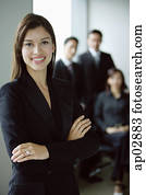 Businesswoman standing with arms crossed, smiling, people in the background   