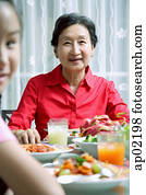 Senior adult at dining table, smiling at camera, granddaughter in the foreground Senior adult at dining table, smiling at camera, granddaughter in the foreground
