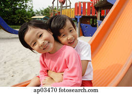 Two young girls sitting on slide, embracing, smiling at camera Two young girls sitting on slide, embracing, smiling at camera