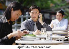 Business people at outdoor café, focus on man with mobile phone