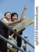 Two women side by side, one pointing in the distance, the other holding map Two women side by side, one pointing in the distance, the other holding map