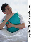 Man sitting in bed, embracing pillow, yawning