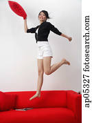 Young woman jumping on sofa, smiling at camera Young woman jumping on sofa, smiling at camera