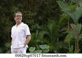 Mature men dressed in white, standing in garden, hands in pockets Mature men dressed in white, standing in garden, hands in pockets