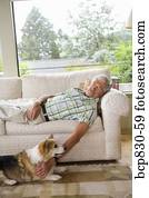 Man napping on a couch with his dog sitting beside him