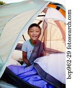 Young boy peeking out from tent on beach at sunrise