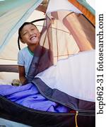 Young boy peeking out from tent on beach at sunrise