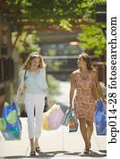 Two friends strolling outdoors and carrying shopping bags. Two friends strolling outdoors and carrying shopping bags.