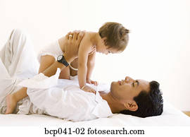 Dad lying on bed holding toddler