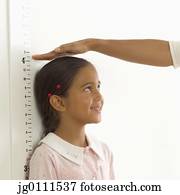 Person measuring a young girls height against a height chart on the wall