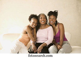 Three women sitting on a couch looking at camera smiling