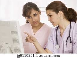 Two nurses discussing in front of a computer monitor