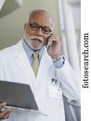 Senior male African doctor talking on cell phone with chart