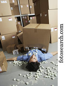 Male warehouse worker laying under fallen box with packing peanuts