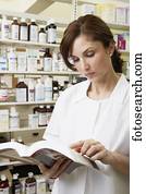 Female pharmacist looking at book in pharmacy
