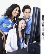 Young Asian female computer service technician with coworkers looking over her shoulder 