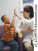 African boy and Hispanic female doctor high-fiving in waiting room