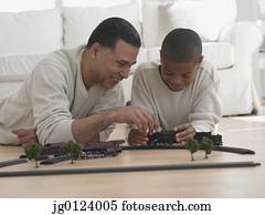 African father and son playing with model train on floor