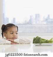 African girl looking at broccoli on table