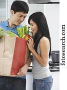 Asian couple looking in grocery bag in kitchen