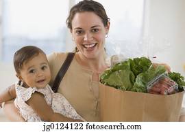 Hispanic mother carrying baby and groceries
