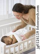 Hispanic mother tucking sleeping baby in crib