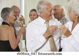 Senior couple toasting at party with friends in background Senior couple toasting at party with friends in background