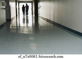 Two people standing at end of corridor in hospital
