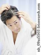 Asian man looking at gray hair in mirror