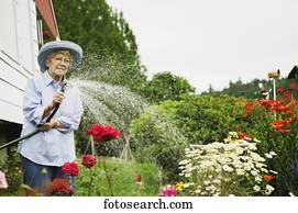 Senior woman watering plants with hose