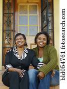 African mother and adult daughter sitting on porch steps