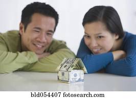 Asian couple looking at house made of money