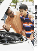 Middle Eastern father and son looking under car hood