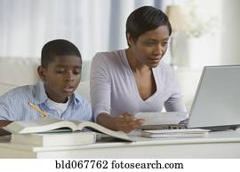 African boy doing homework next mother on computer