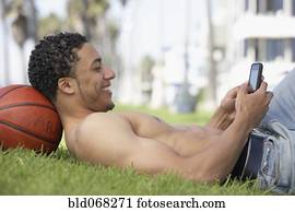 Young mixed race man with bare chest on grass with cell phone