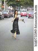 Barefoot Asian woman in evening gown running in street