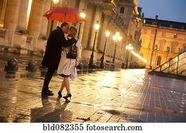 Caucasian couple kissing in rain at night at the Louvre