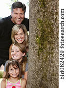 Smiling Caucasian family near tree trunk