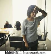 Businesswoman leaning wall with co-workers in background