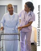 Nurse helping woman use walker in hospital hallway