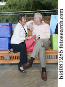 Senior Hispanic couple sitting on bench with gifts Senior Hispanic couple sitting on bench with gifts