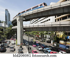 A mass transit train on an elevated track passes modern building