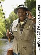 African man in fishing vest using cell phone