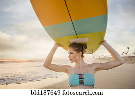 Caucasian woman carrying surfboard on beach