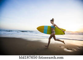 Caucasian woman carrying surfboard on beach