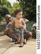 Father adjusting toddler son's shorts in park