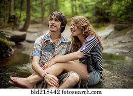 Couple sitting barefoot on boulders in forest