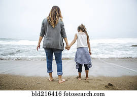Hispanic mother and daughter standing barefoot on beach