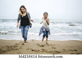 Hispanic mother and daughter walking barefoot on beach